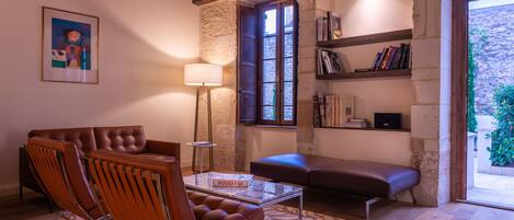 A cozy living room with a leather sofa, a glass coffee table, and a bookshelf.