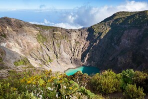 Un cratère abritant un lac turquoise, entouré d’un paysage accidenté et d’une végétation luxuriante.