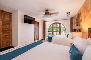 Habitación de hotel con dos camas, un ventilador de techo, un ventanal arqueado grande y una puerta de madera con un panel decorativo.
