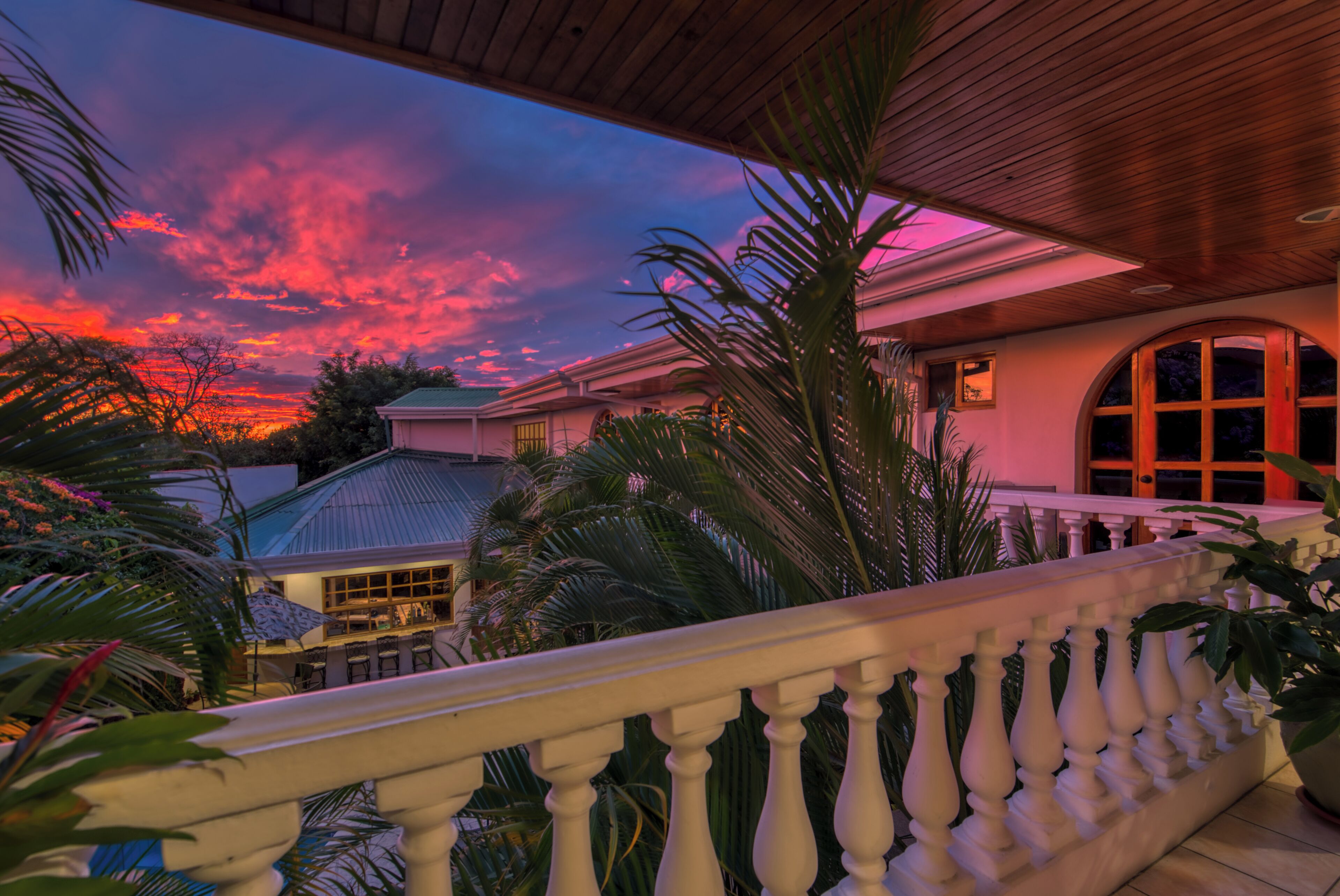 Un balcón con vista a una casa y un atardecer.