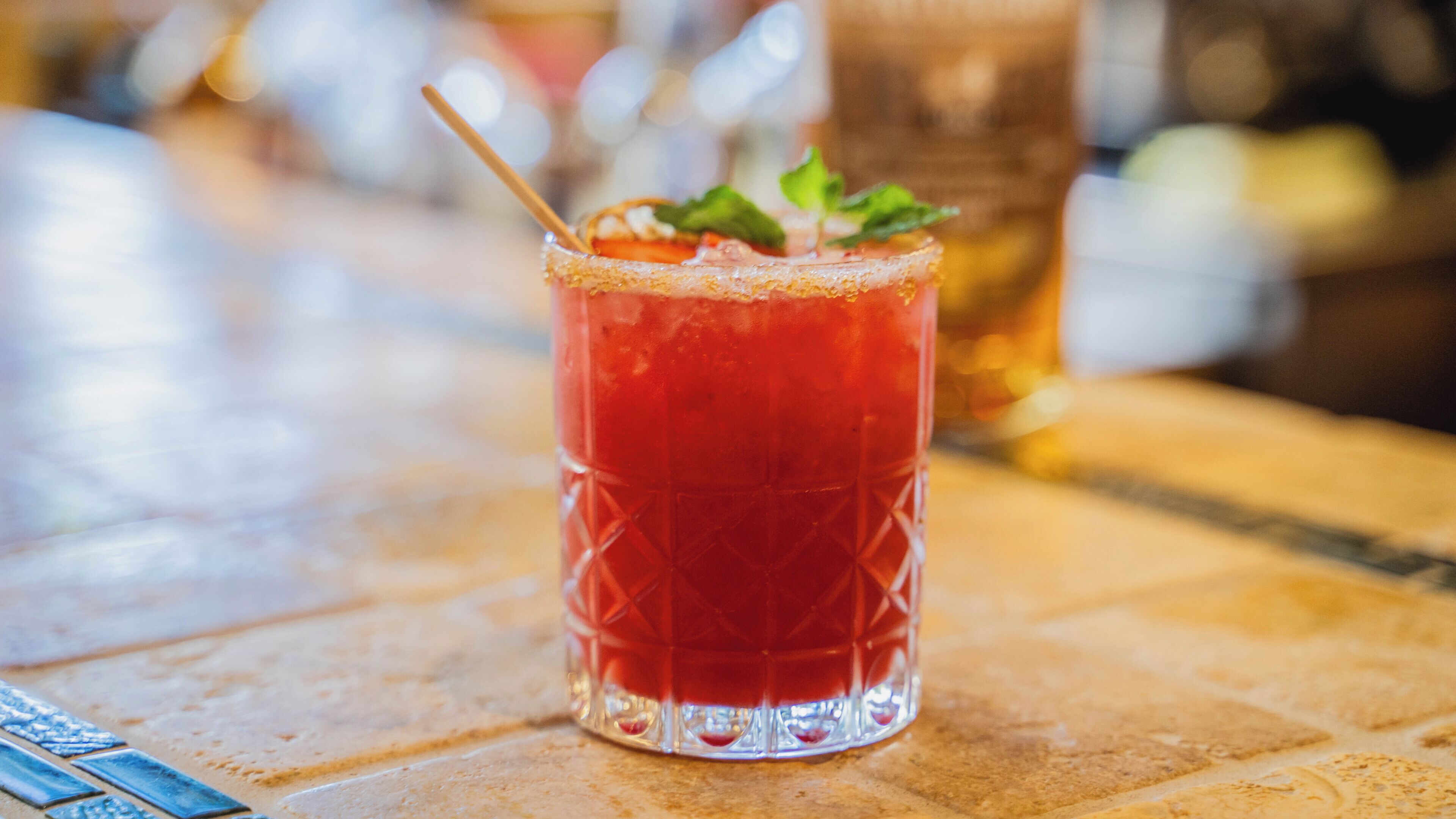 A clear glass with a red beverage, a straw, and a mint garnish on a bar counter.