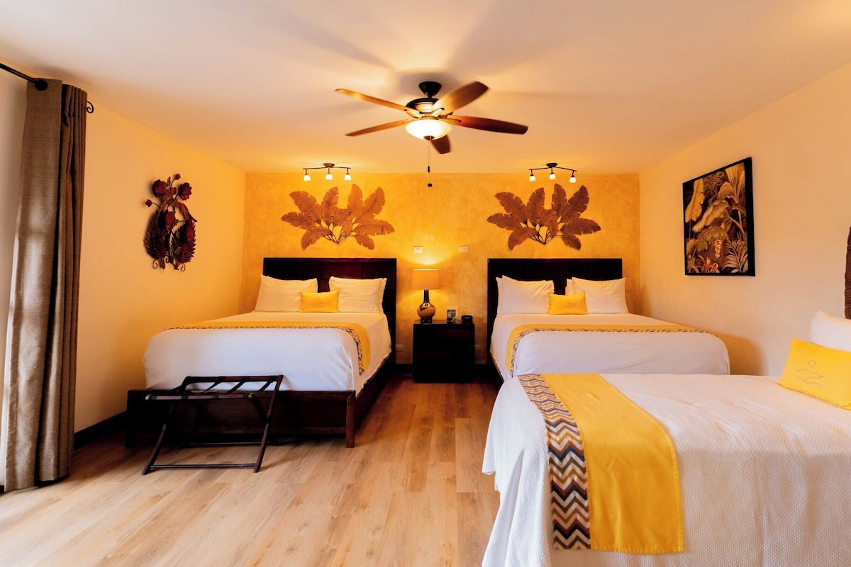 Une chambre d’hôtel avec deux lits, un ventilateur de plafond, des œuvres d’art murales et un plancher en bois.