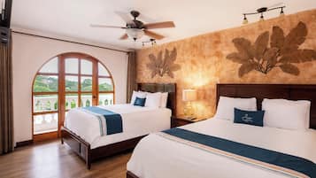 Habitación de hotel con dos camas, ventilador de techo, ventana grande y un mural en la pared.