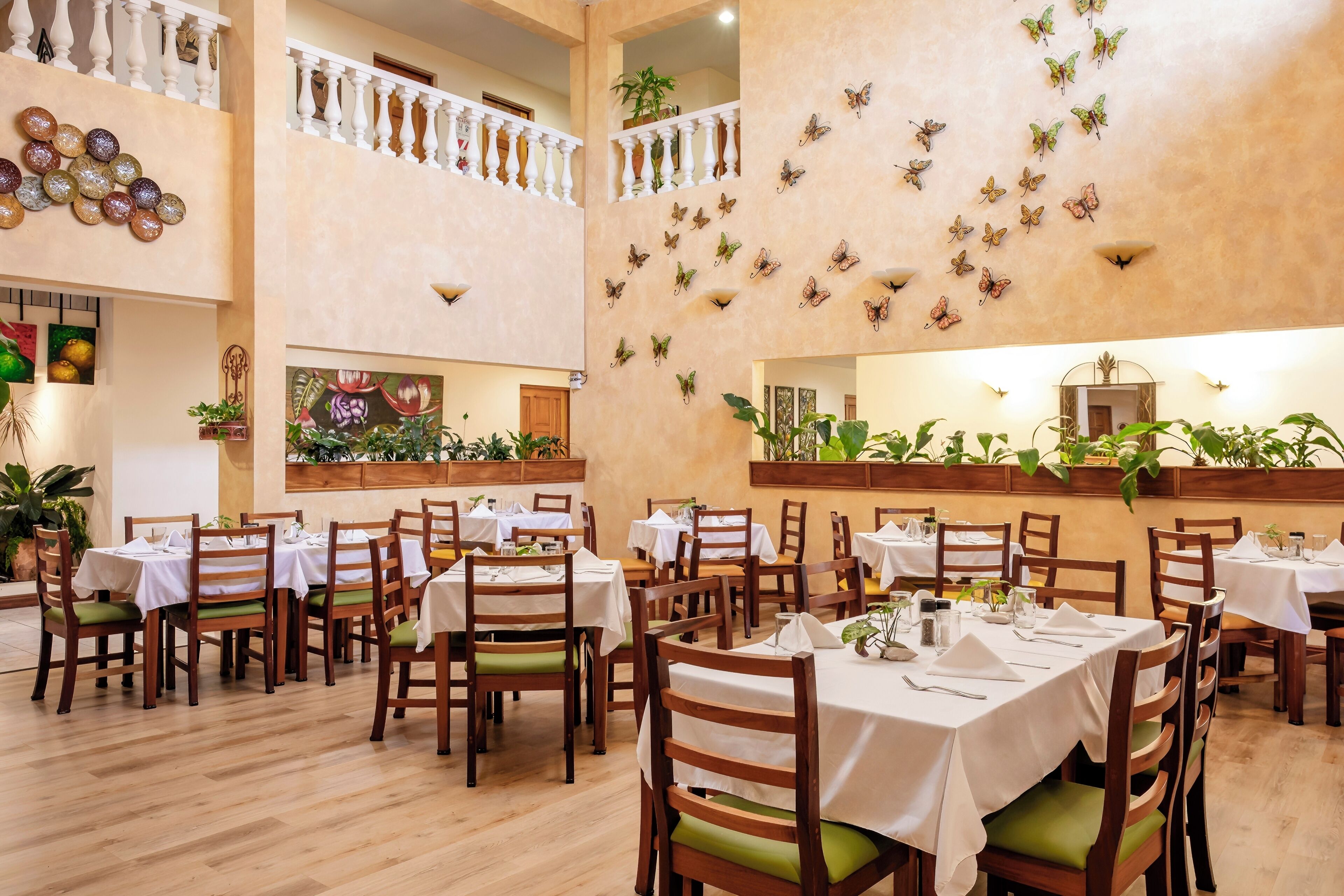 A dining area with multiple tables and chairs, a decorative wall with butterfly wall art, and a ceiling with a light fixture.