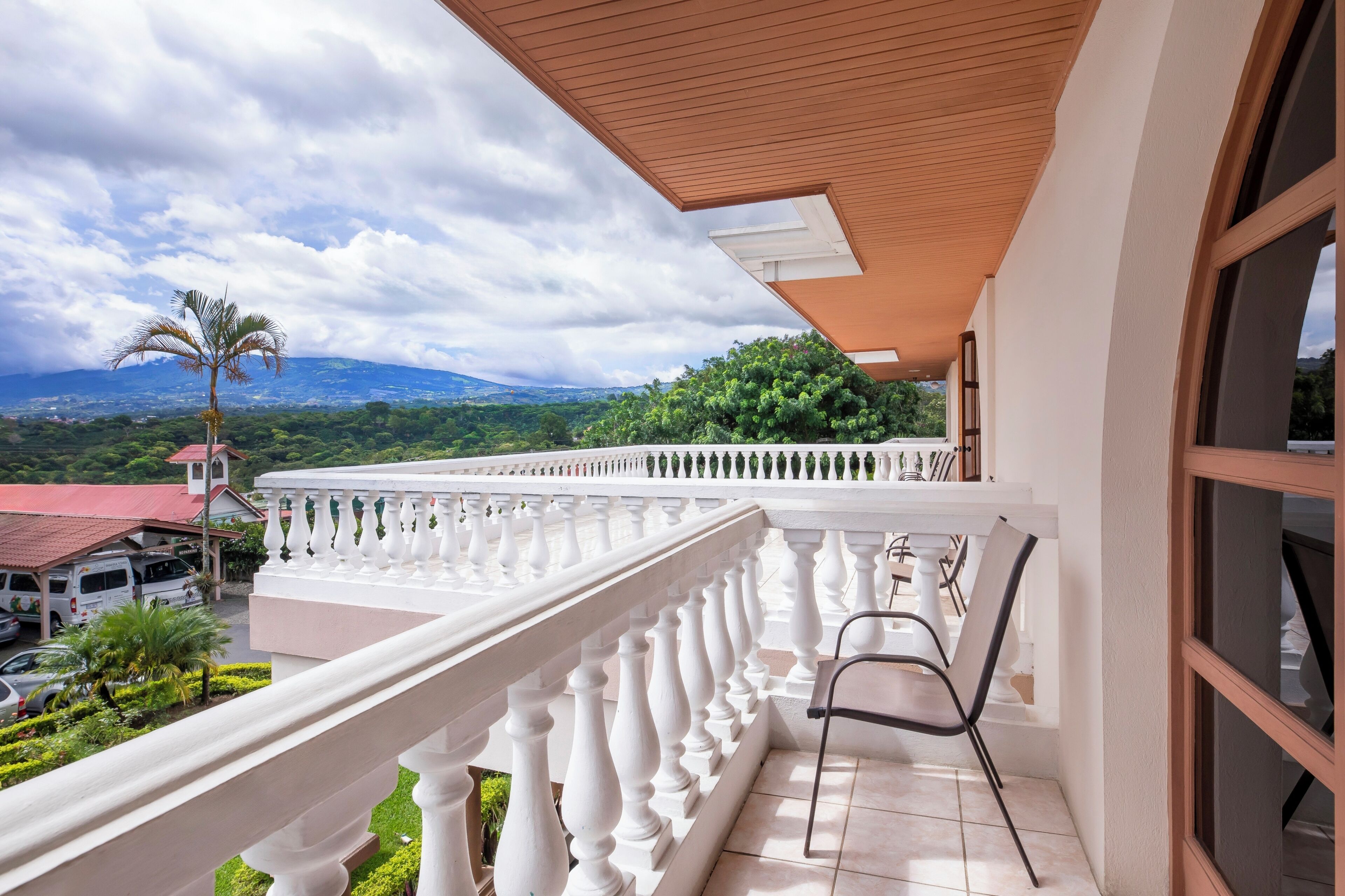 Un balcón con barandilla blanca, una silla y vistas a un paisaje montañoso.