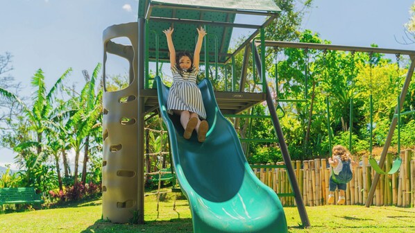 Une aire de jeux avec un toboggan vert et une structure d’escalade.