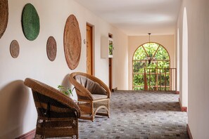 A hallway with wicker furniture, a patterned carpet, and a large arched window with a view of greenery.