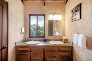A bathroom with two sinks, a large mirror, and a window with a view of trees.
