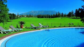 Una piscina con sillas de descanso y vistas a un campo verde y montañas.