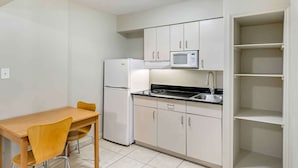 Een kleine keuken met witte kastjes, een magnetron, een koelkast en een eettafel met stoelen.