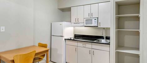 Cocina compacta con armarios blancos, microondas, refrigerador y mesa de comedor con sillas.