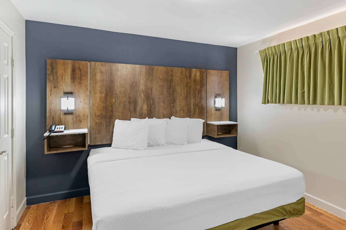 A hotel room with a large bed, wooden headboard, bedside tables with lamps, and a green curtain.
