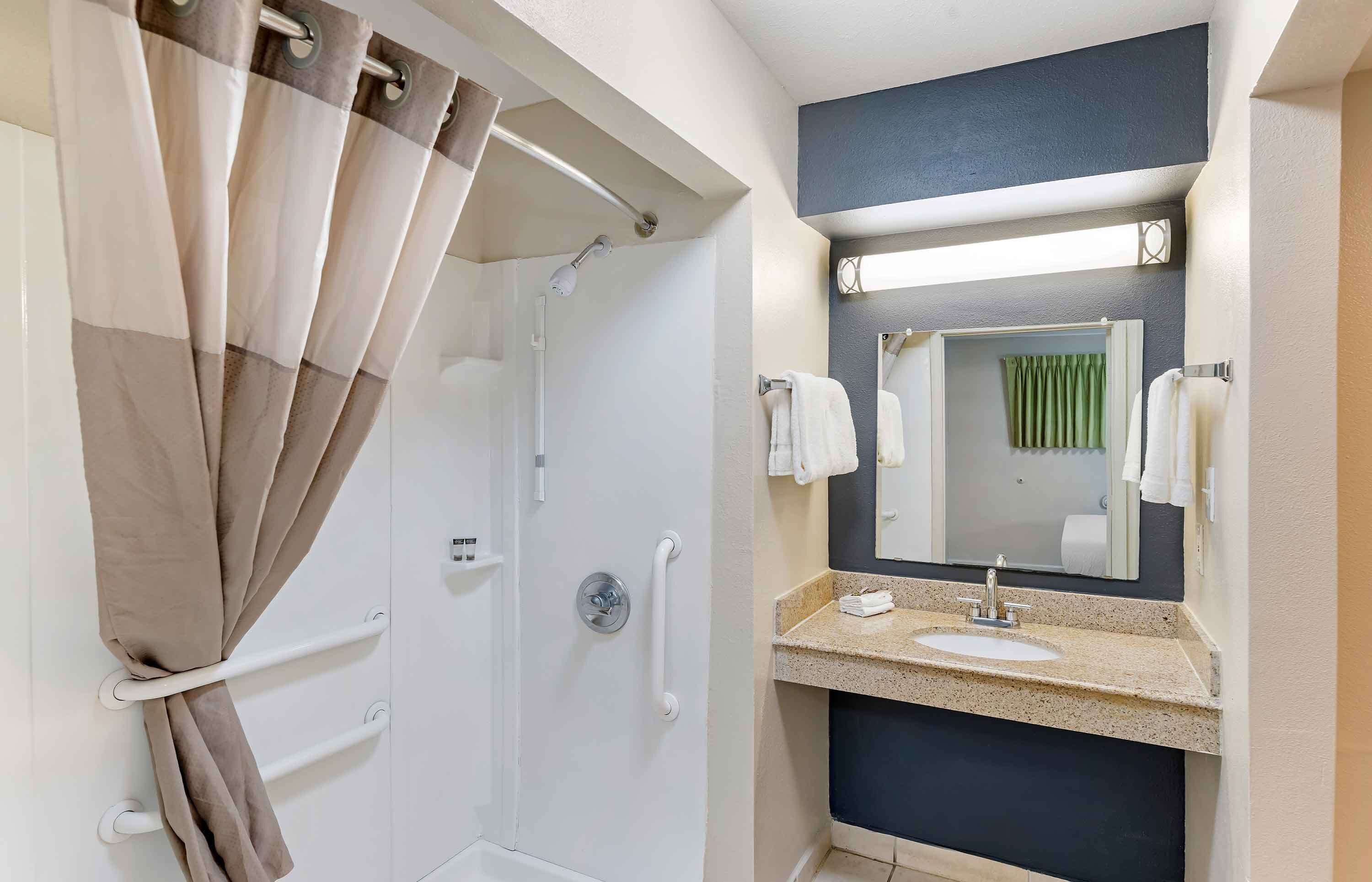 A bathroom with a shower, a sink, a mirror, and a towel rack.