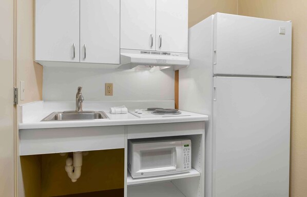 A compact kitchen with white cabinets, a stainless steel sink, a microwave, and a white refrigerator.