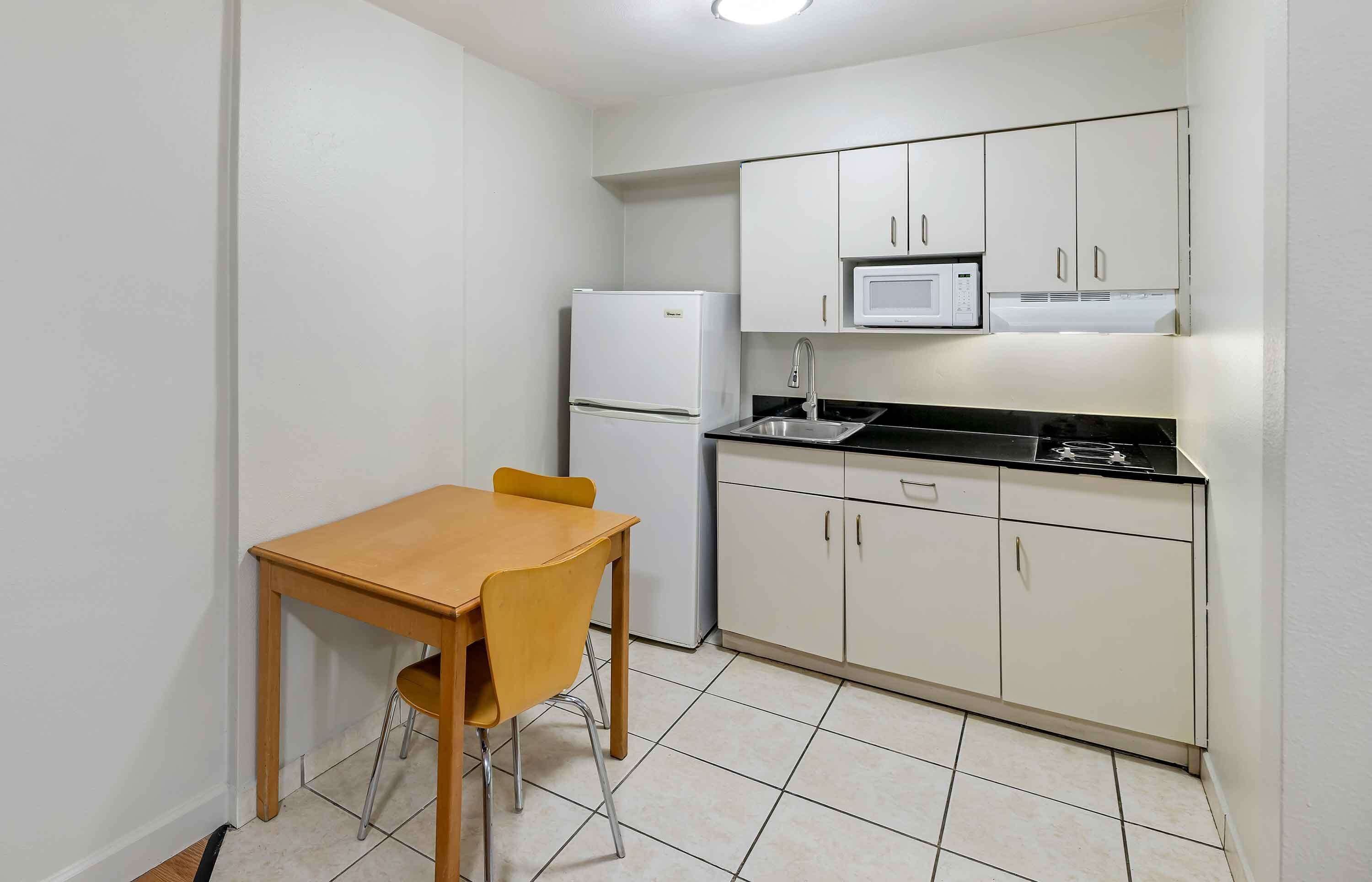 A compact kitchen with white cabinets, a microwave, a refrigerator, and a wooden table with two chairs.