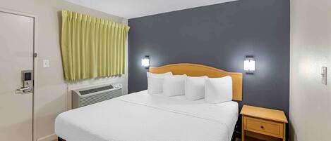Une chambre d’hôtel avec un lit, une table de chevet, un radiateur fixé au mur et une porte avec une serrure.