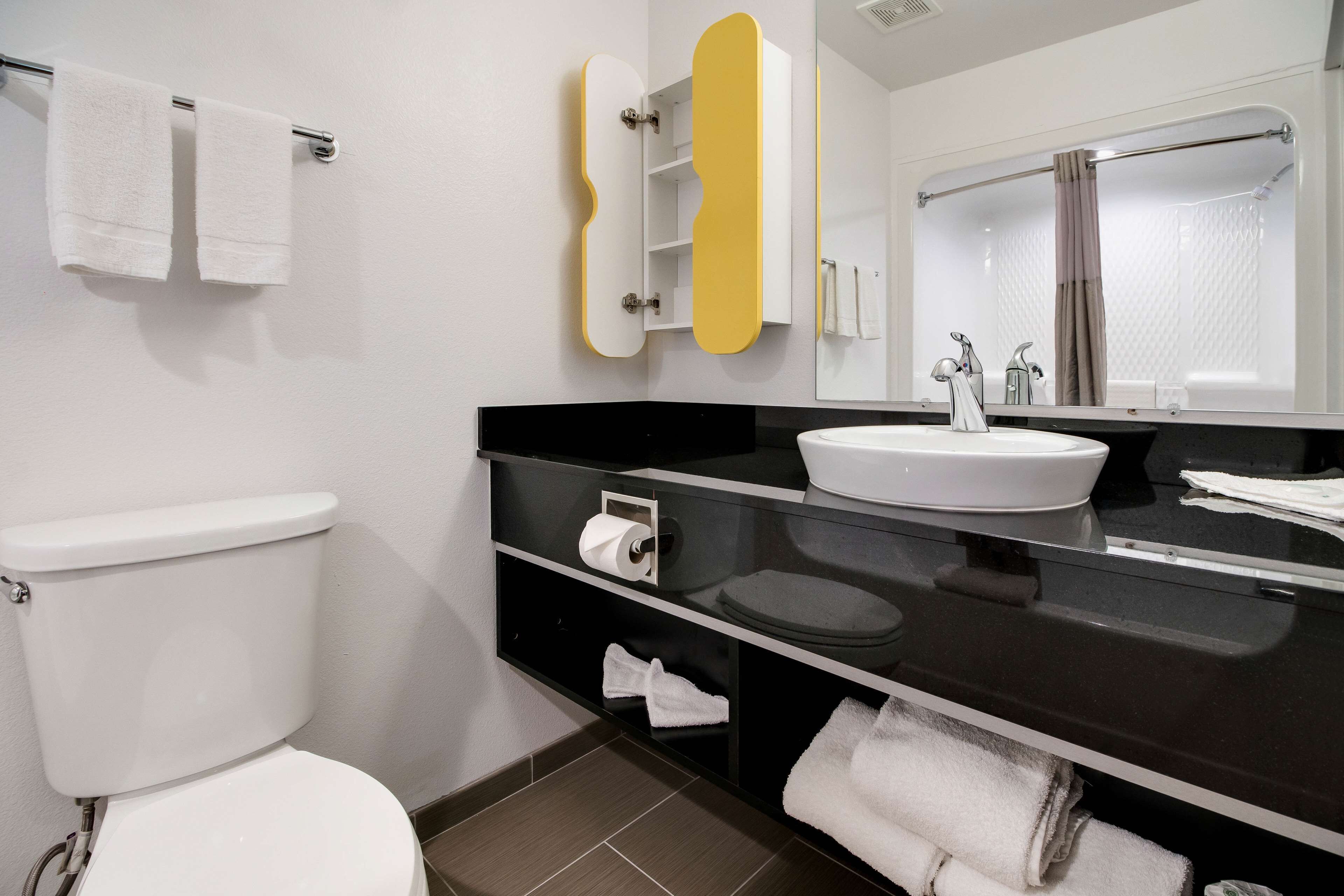A modern bathroom with a white toilet, a black vanity with a sink, and a mirror.