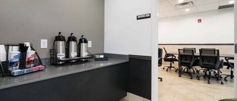 A reception area with a coffee station, a conference room with chairs and tables, and a sign indicating the conference room.