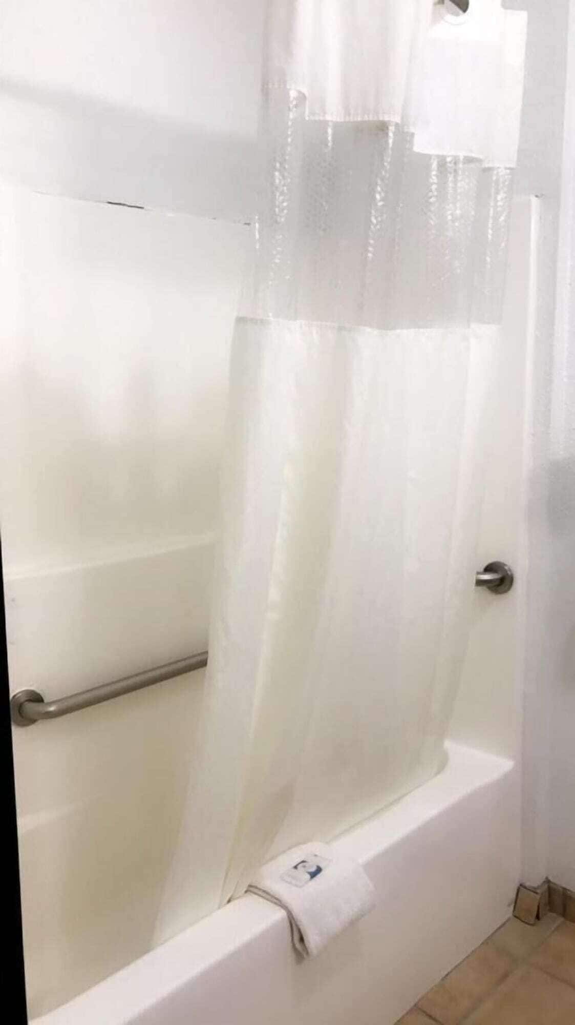 Una bañera blanca con cortina de ducha, toallero y manija.