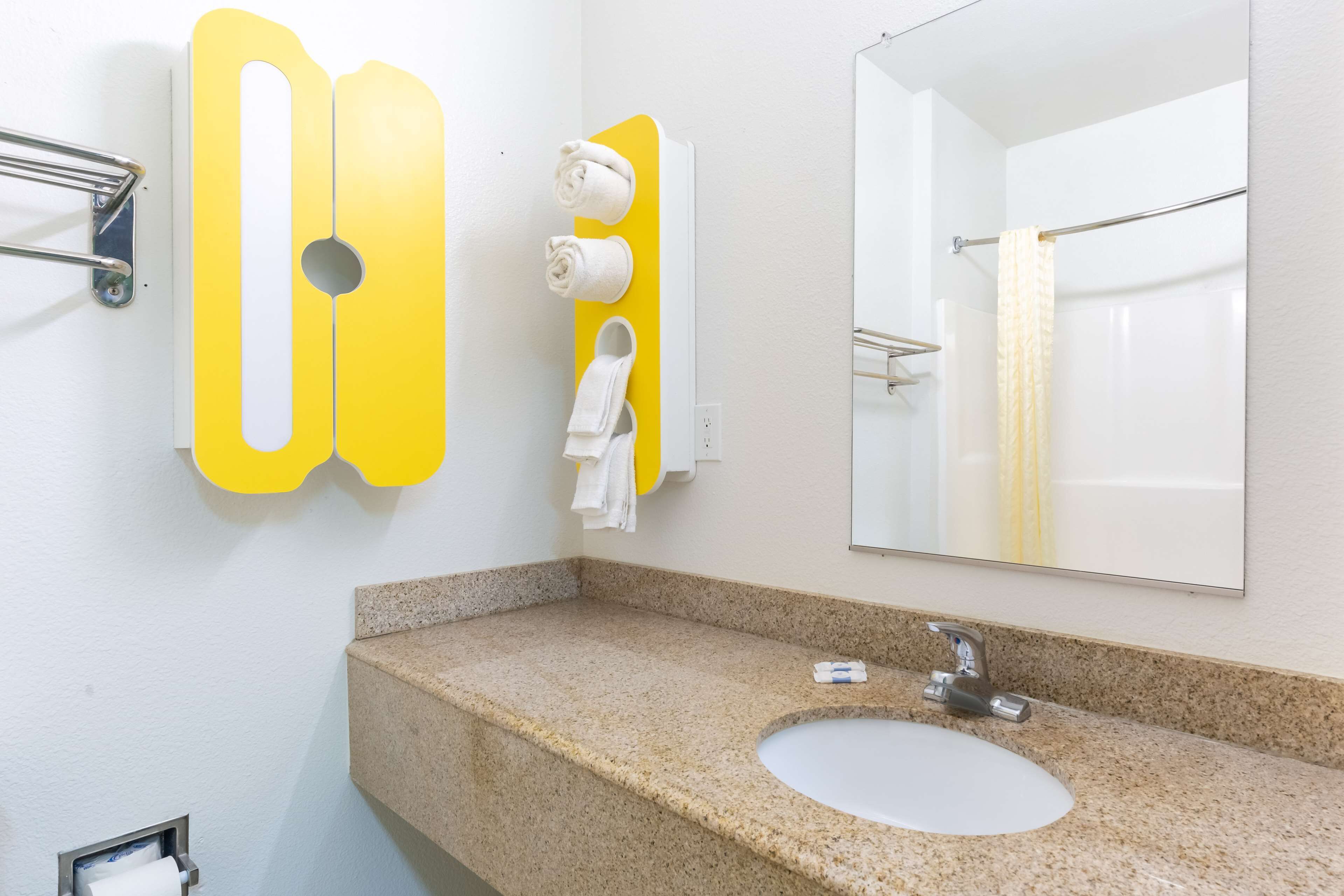 Un baño con encimera de granito, un lavamanos, un espejo y barras para toallas.