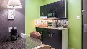 Cocina compacta con microondas, tostadora y cafetera en la encimera, una mesa de comedor con sillas y una lámpara de pared.
