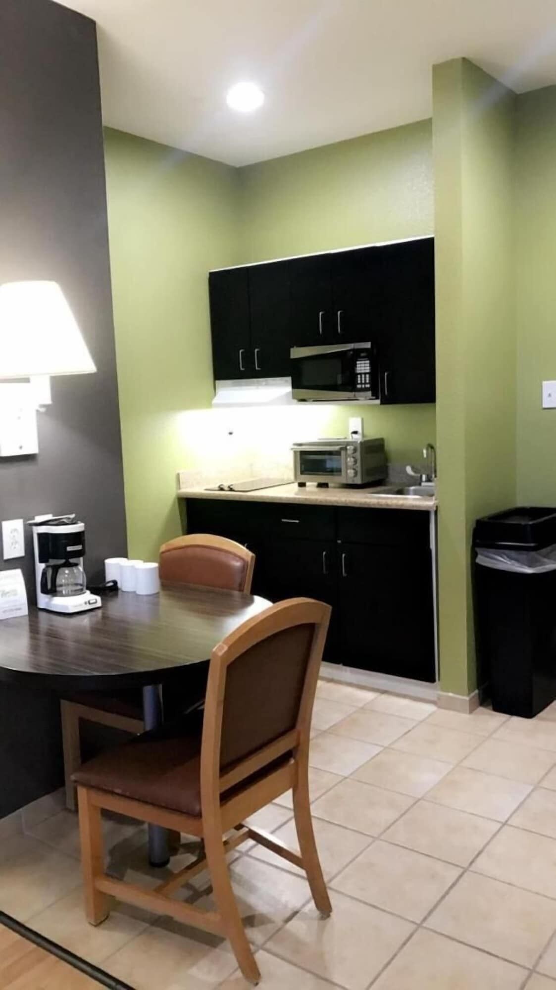 A compact kitchen with a dining table and chairs, a coffee maker, and a microwave.