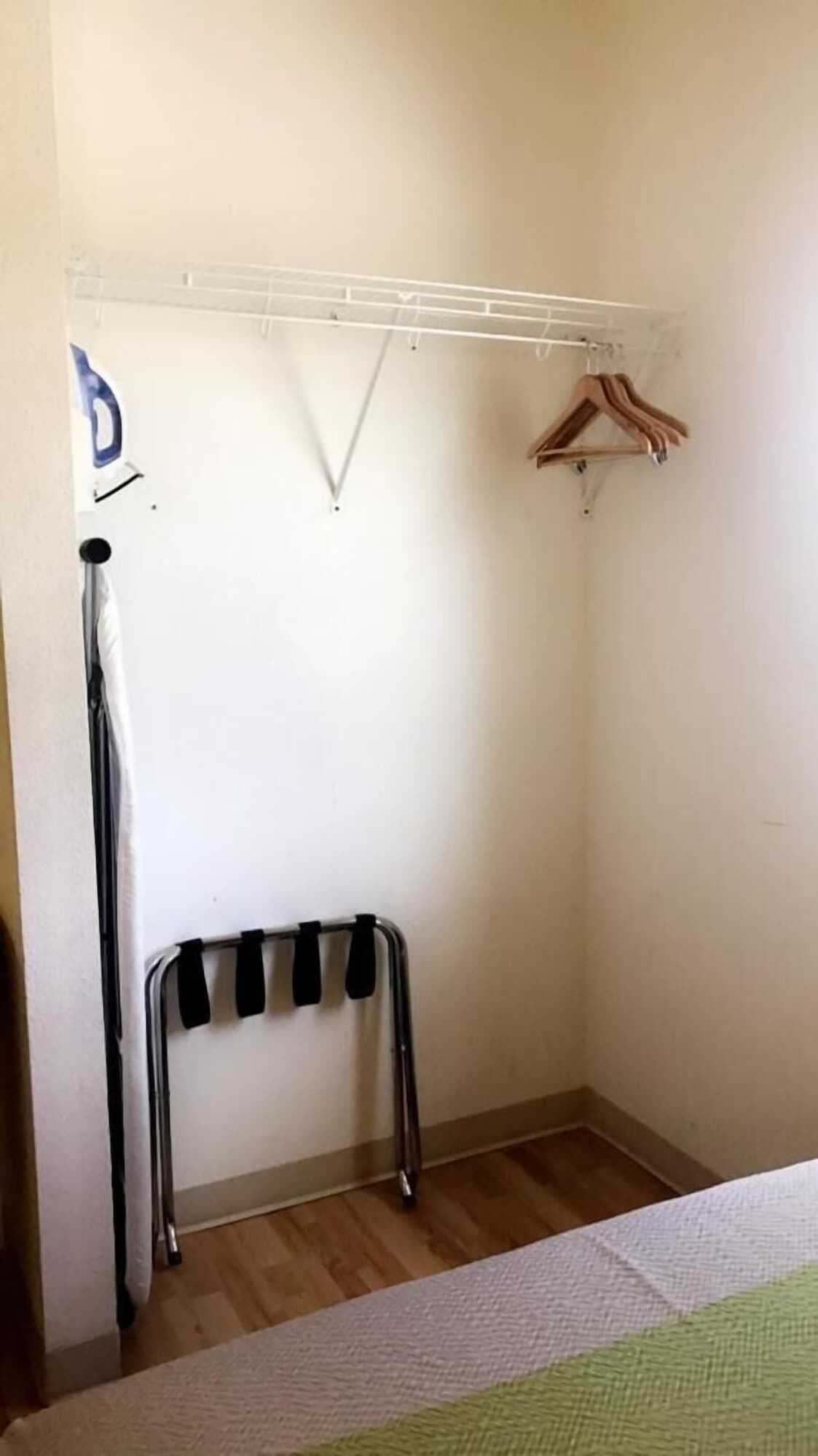 A small, narrow room with a wooden floor, a metal bench, a white wall, and a clothes rack.
