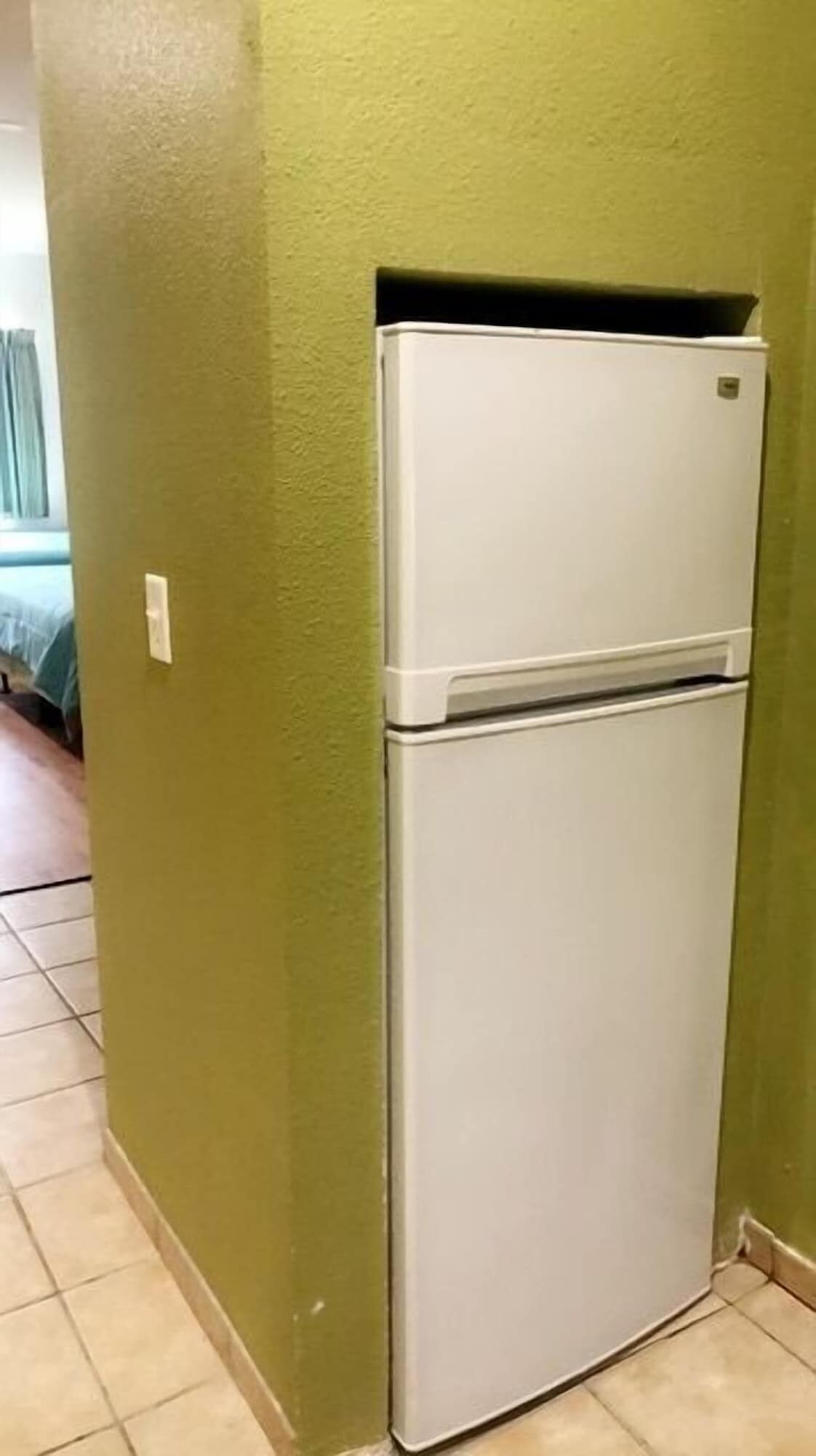 A white refrigerator in a room with green walls and tiled flooring.