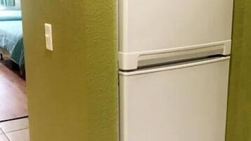 A white refrigerator in a room with green walls and tiled flooring.