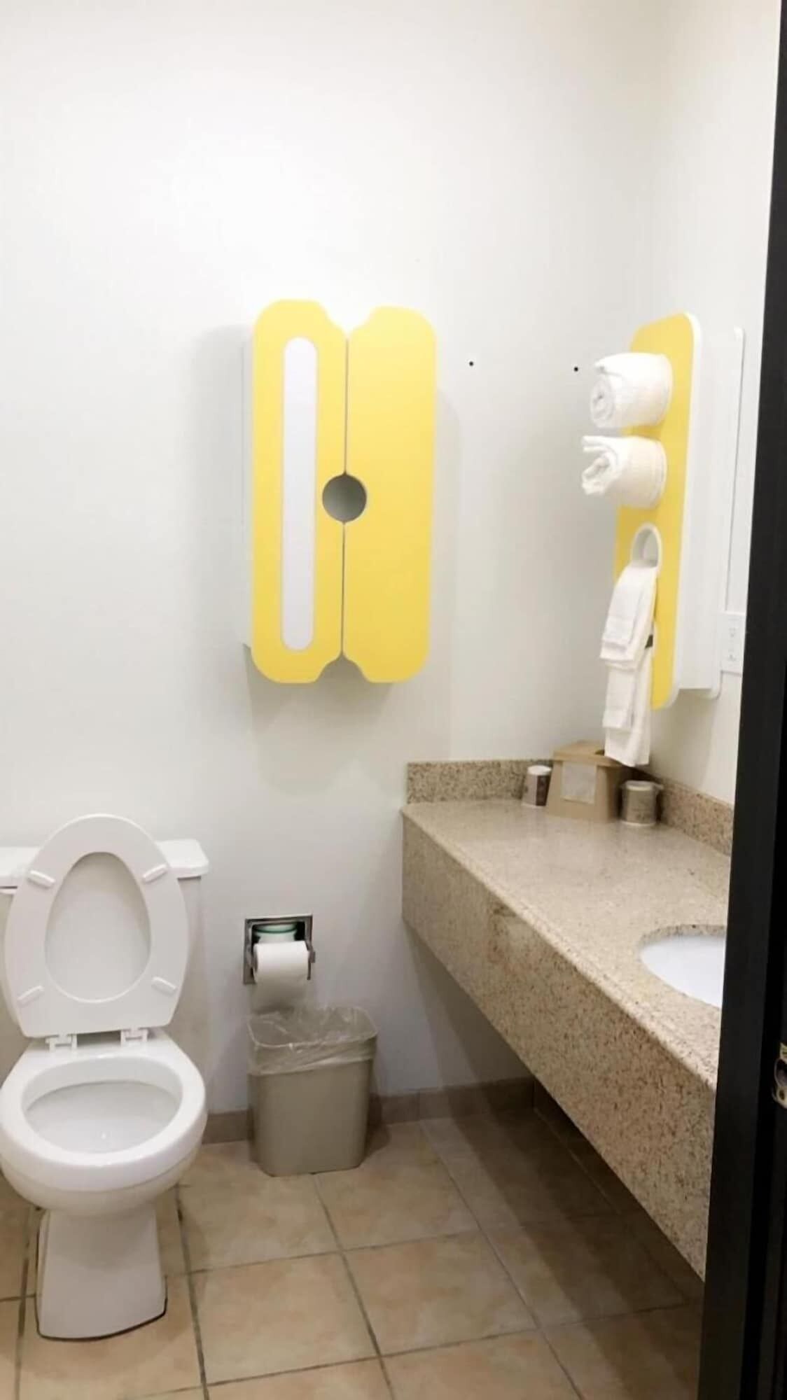 A small bathroom with a toilet, a trash bin, a towel dispenser, and a sink.