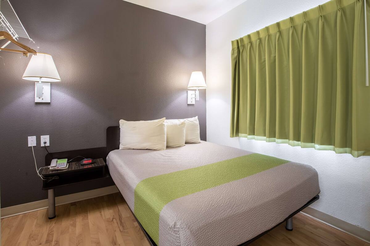 A hotel room with a bed, bedside lamps, a nightstand, and a window with curtains.