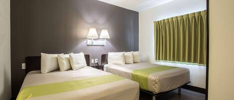 Une chambre d’hôtel avec deux lits, une table de chevet, une lampe et une fenêtre avec des rideaux.