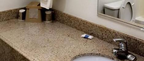 A bathroom with a granite countertop, a sink, a mirror, and a towel dispenser.