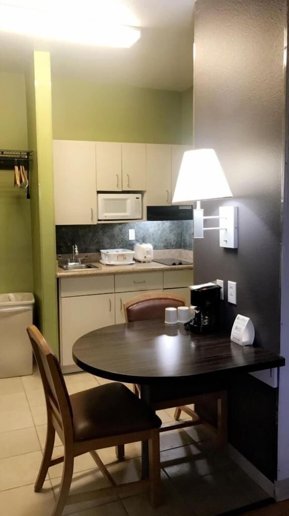 A compact kitchen with white cabinets, a microwave, a toaster, and a table with chairs.