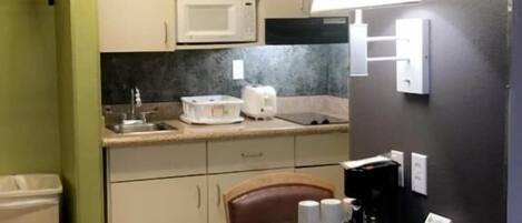 A compact kitchen with white cabinets, a microwave, a toaster, and a table with chairs.