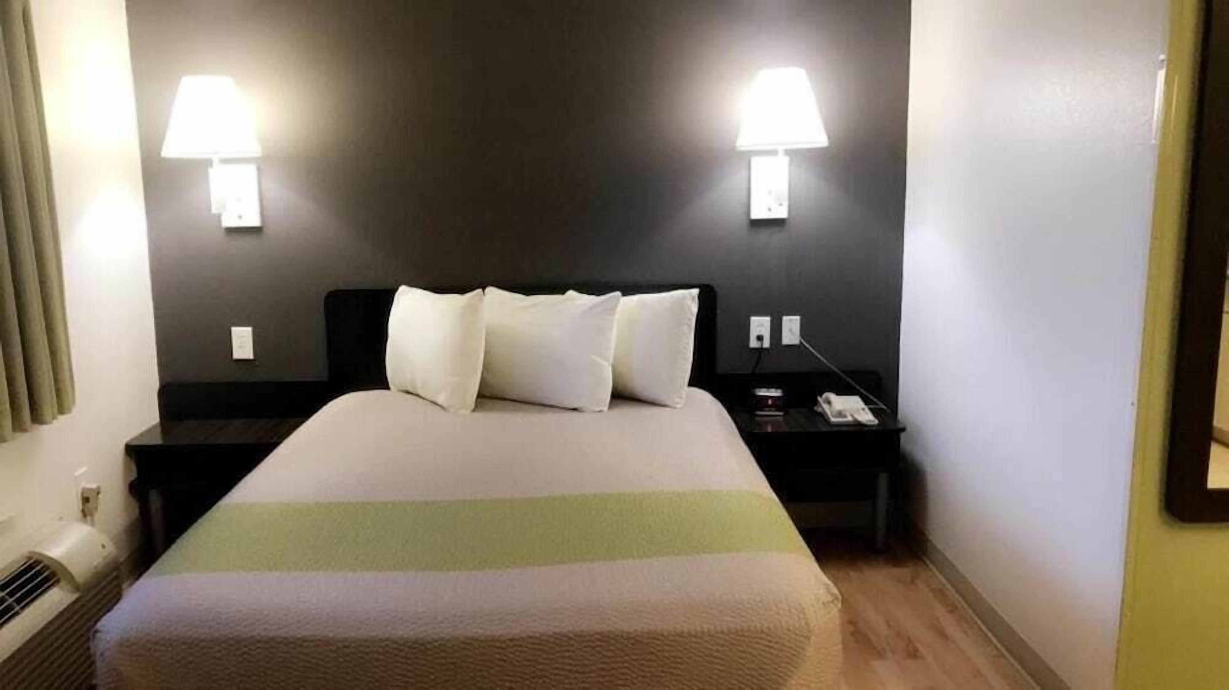 A hotel room with a large bed, two bedside tables, a nightstand, and two wall-mounted lamps.