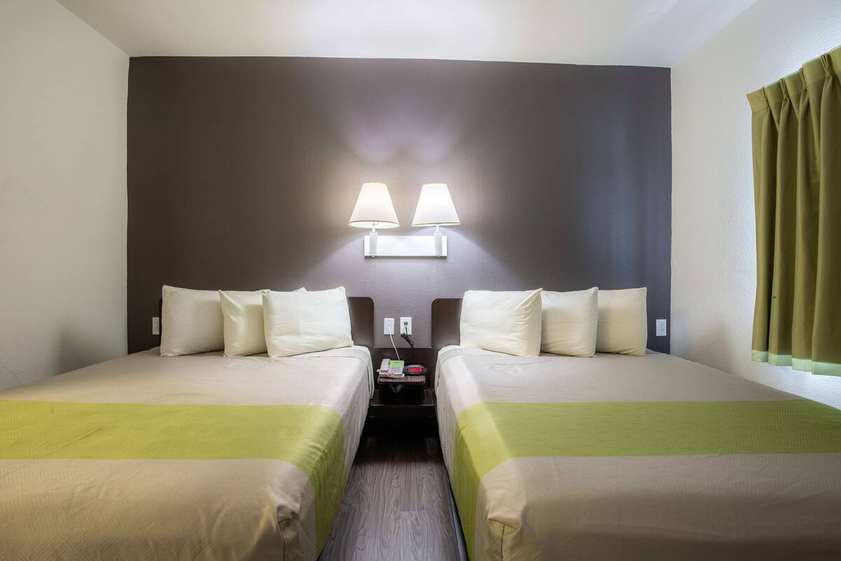 A hotel room with two beds, a nightstand, and a wall-mounted lamp.
