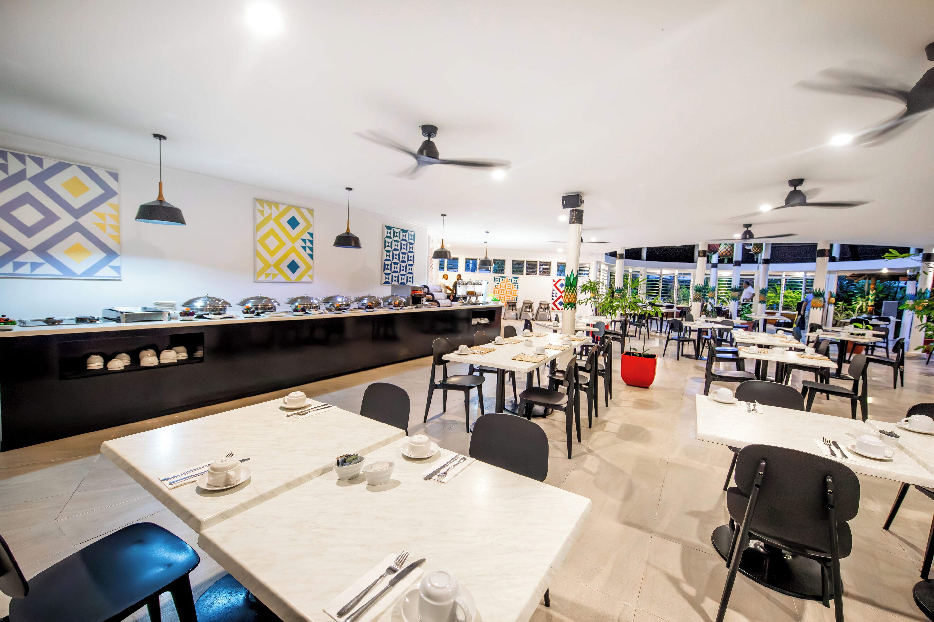 Un comedor moderno con varias mesas y sillas, ventiladores de techo y decoración en las paredes.