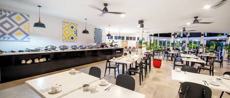 Un comedor moderno con varias mesas y sillas, ventiladores de techo y decoración en las paredes.