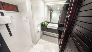 Un baño moderno con cabina de ducha de vidrio, un lavabo blanco y un mueble de tocador de madera oscura.