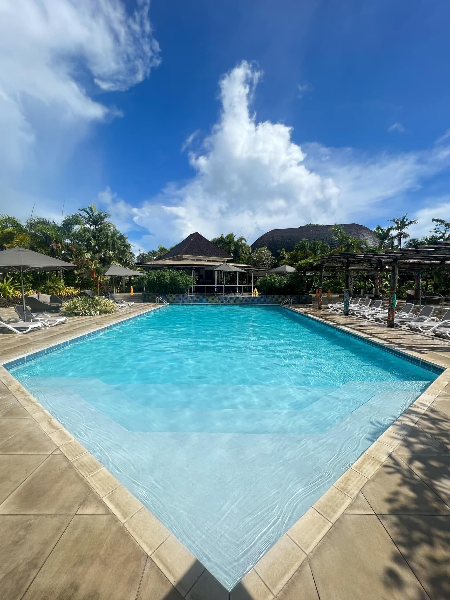 Una piscina al aire libre, sombrillas, sillones reclinables de piscina