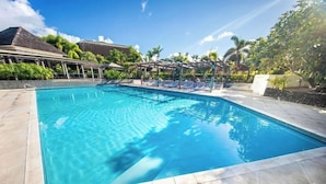 A rectangular swimming pool with clear blue water, surrounded by a tiled deck and a covered seating area with lounge chairs. - Tanoa Tusitala Hotel (Apia)