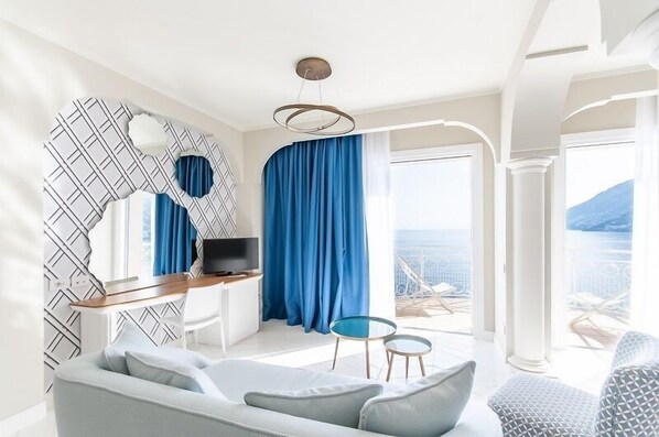 A modern living room with a sofa, a TV, and a balcony with blue curtains.