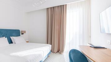Une chambre d’hôtel équipée d’un lit, d’un bureau, d’une chaise, d’une fenêtre avec des rideaux et d’un luminaire au plafond.