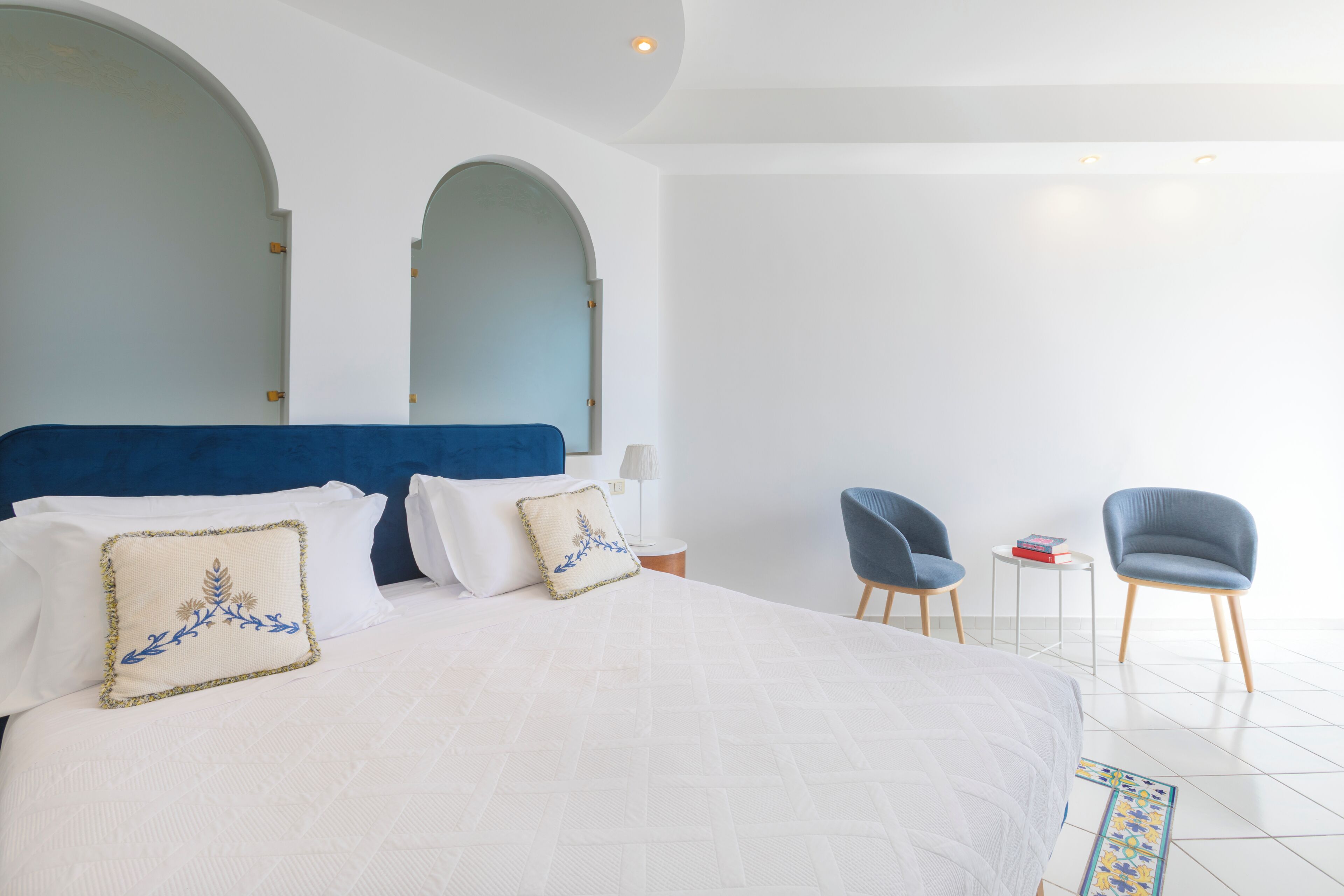 Ein Hotelzimmer mit einem großen Bett, zwei Stühlen, einem kleinen Tisch und einem Nachttisch.