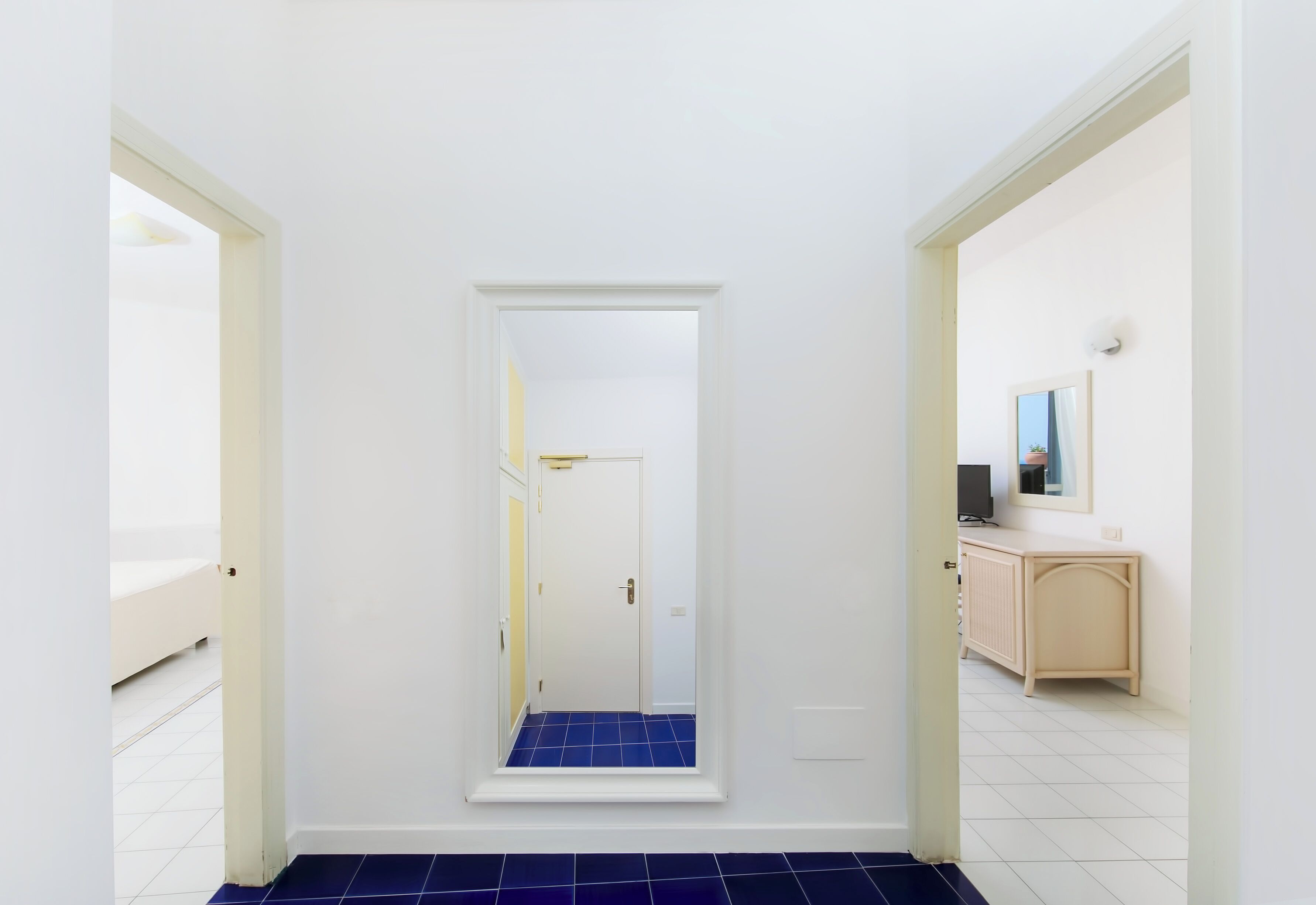 A hallway with a white door, a blue-tiled floor, and a light-colored console table with a mirror.