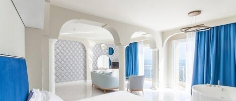 A modern hotel room with a large bed, a sitting area with a chair, a bathtub, and a view of the outdoors.