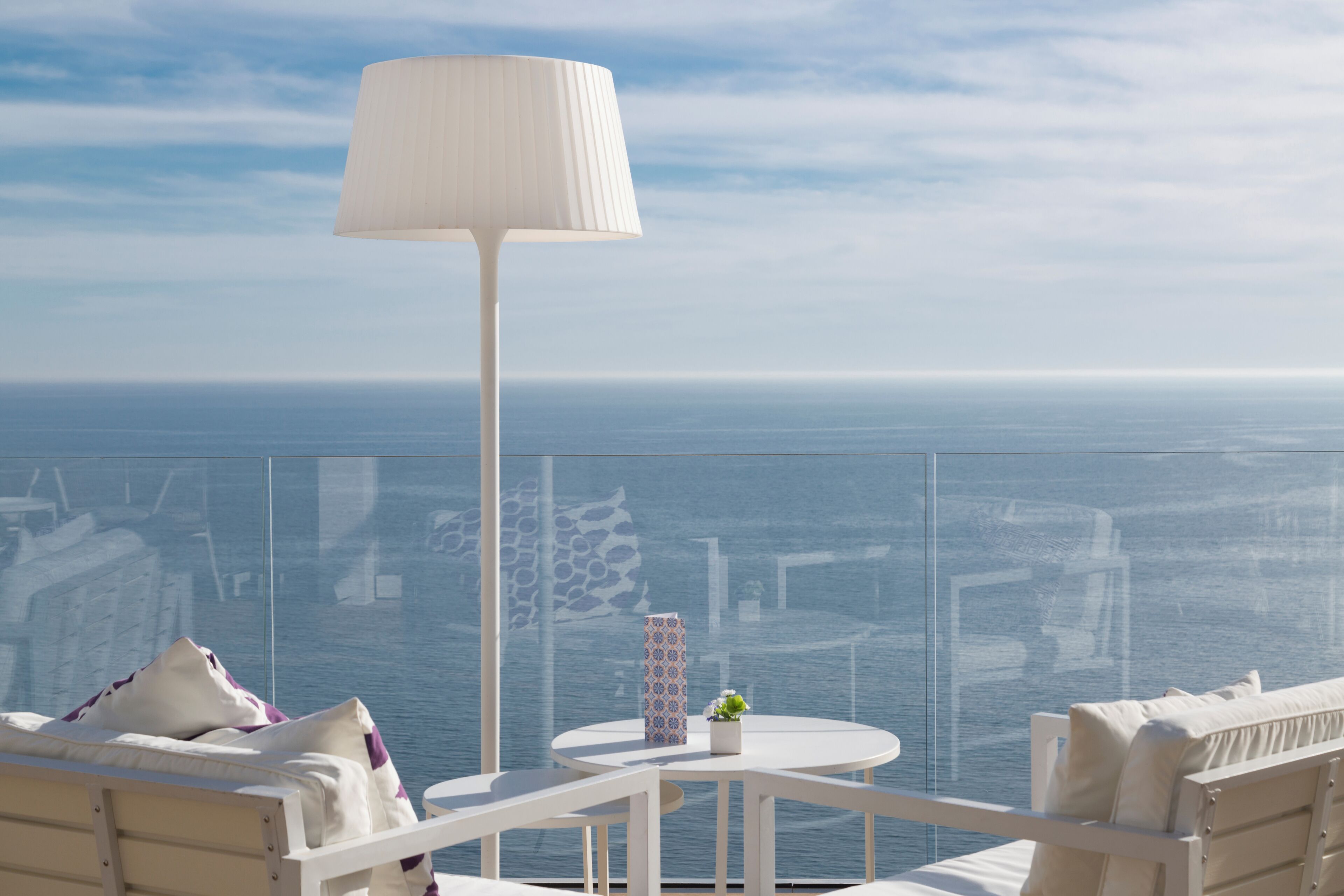 Un balcone con un tavolo bianco, una lampada e vista sul mare.