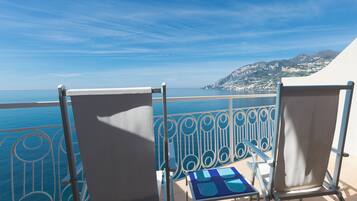 A balcony with two chairs and a small table, overlooking a coastal view with a clear sky.