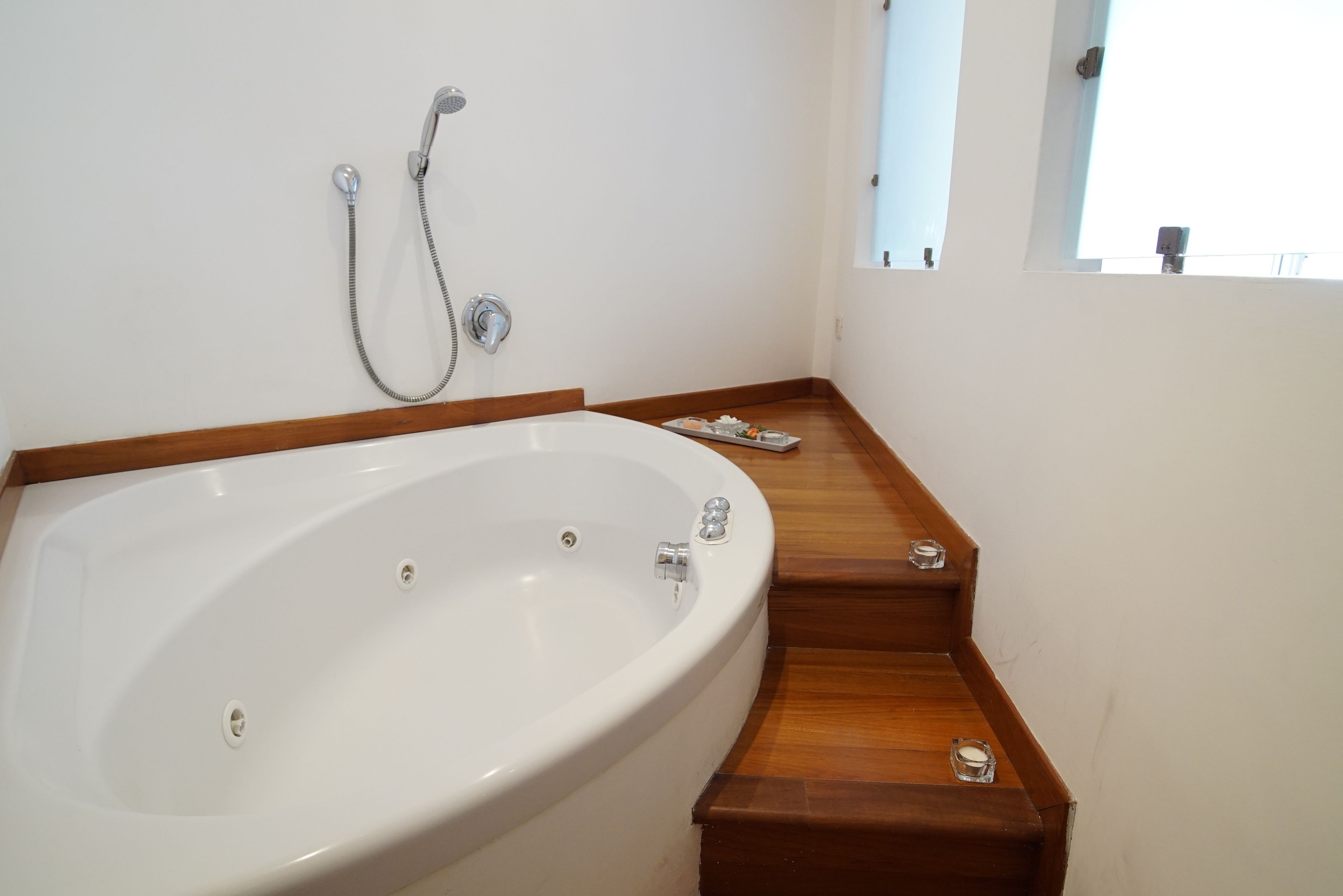 A bathroom with a large white bathtub, wooden steps, and a showerhead.